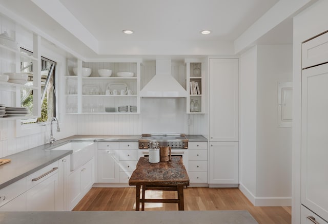 kitchen with wall chimney range hood, sink, light hardwood / wood-style flooring, tasteful backsplash, and white cabinets