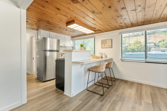 kitchen with kitchen peninsula, a kitchen breakfast bar, stainless steel refrigerator, white cabinets, and wooden ceiling