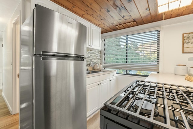 kitchen with wood ceiling, light wood-type flooring, stainless steel fridge, white cabinetry, and gas range