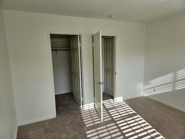 unfurnished bedroom with a walk in closet, a closet, and dark colored carpet