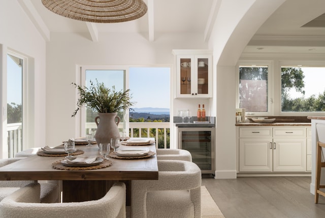 dining room featuring beverage cooler, bar, light wood-type flooring, a mountain view, and beam ceiling