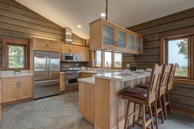 kitchen with light countertops, vaulted ceiling, a sink, wooden walls, and high quality appliances