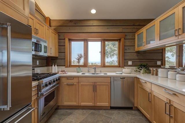 kitchen featuring wooden walls, high end appliances, glass insert cabinets, a sink, and recessed lighting