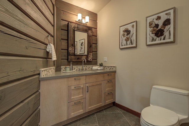 half bath with baseboards, vanity, toilet, and tile patterned floors