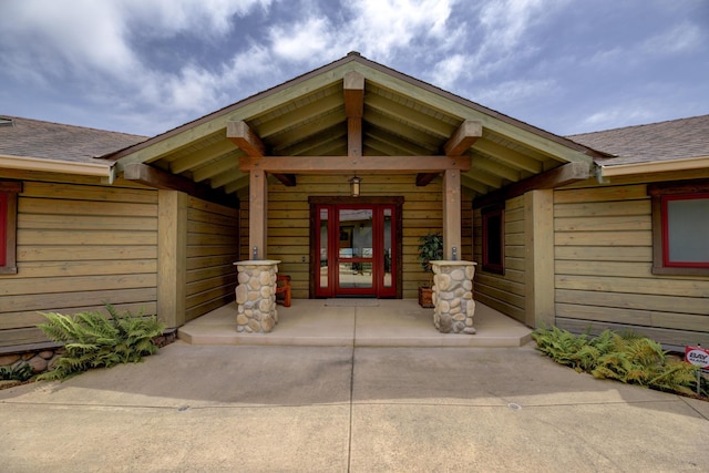 doorway to property with covered porch and a shingled roof