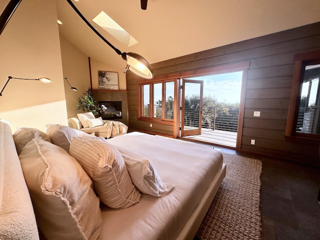 bedroom featuring lofted ceiling with skylight, wood walls, a tile fireplace, and access to exterior