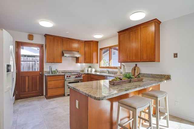 kitchen with stainless steel stove, a kitchen bar, white refrigerator with ice dispenser, kitchen peninsula, and light stone countertops