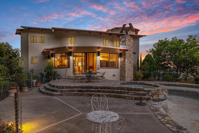 back house at dusk featuring a patio and an in ground hot tub