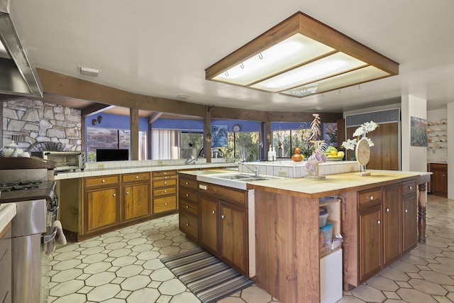 kitchen featuring sink, a center island with sink, wall chimney range hood, and wood counters