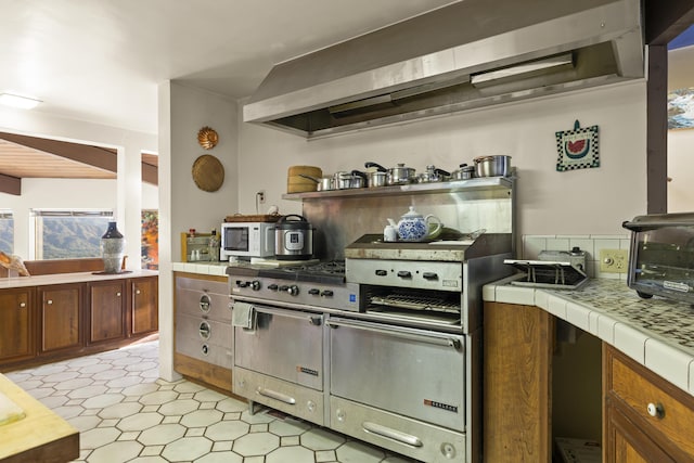 kitchen with wall chimney exhaust hood and tile counters