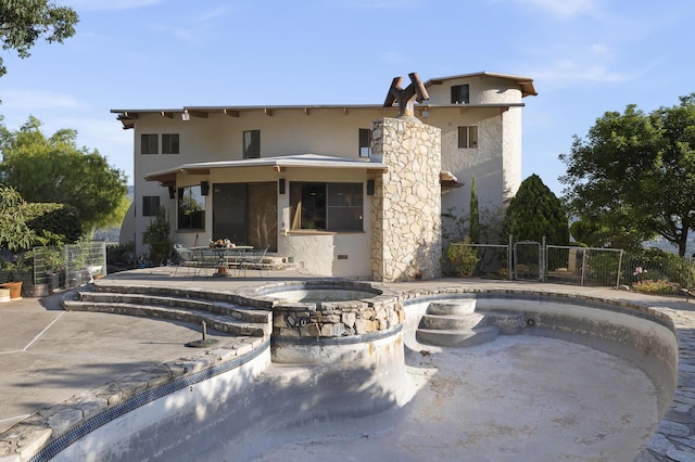 rear view of property featuring a patio and an in ground hot tub