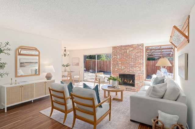 living room featuring a brick fireplace, a textured ceiling, hardwood / wood-style floors, and a chandelier