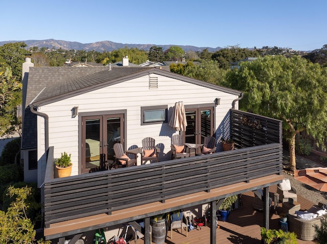 rear view of property featuring a deck with mountain view, outdoor dining area, an outdoor hangout area, french doors, and a chimney