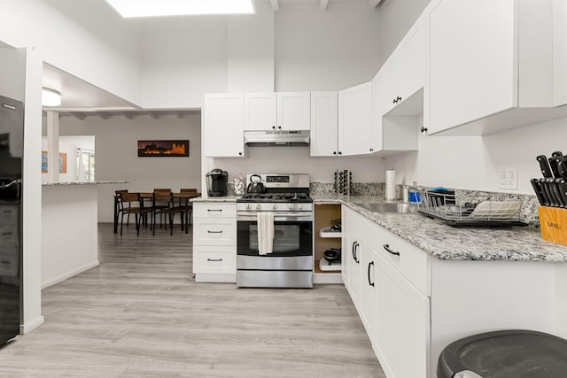 kitchen with gas stove, a towering ceiling, light stone countertops, light hardwood / wood-style floors, and white cabinets