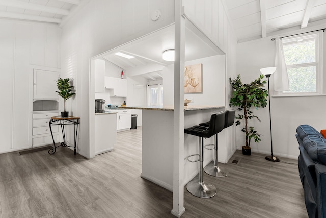 kitchen with light stone countertops, vaulted ceiling with beams, white cabinets, and light hardwood / wood-style floors