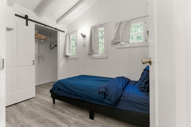 bedroom with multiple windows, a barn door, vaulted ceiling with beams, and light wood-type flooring