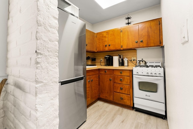 kitchen featuring white range with gas stovetop, stainless steel fridge, and light hardwood / wood-style flooring