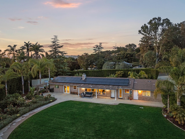 back house at dusk with a patio, a lawn, and solar panels