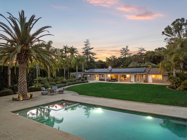 pool at dusk featuring a patio and a lawn