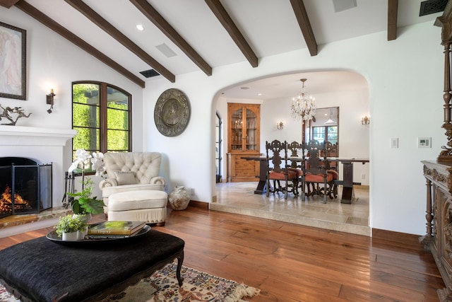 living room with a notable chandelier, beam ceiling, plenty of natural light, and wood-type flooring