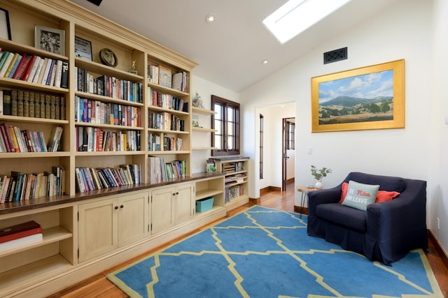 living area with lofted ceiling with skylight and light wood-type flooring