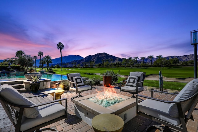 patio terrace at dusk featuring a lawn, an outdoor fire pit, and a mountain view