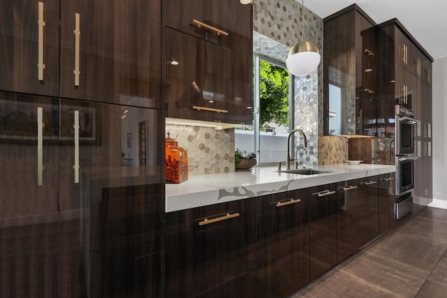 kitchen with dark brown cabinetry, light stone counters, stainless steel double oven, and sink