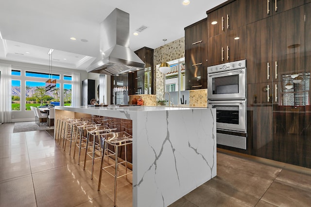 kitchen with light stone counters, a large island with sink, double oven, and island range hood