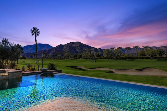 pool at dusk featuring a mountain view and a yard