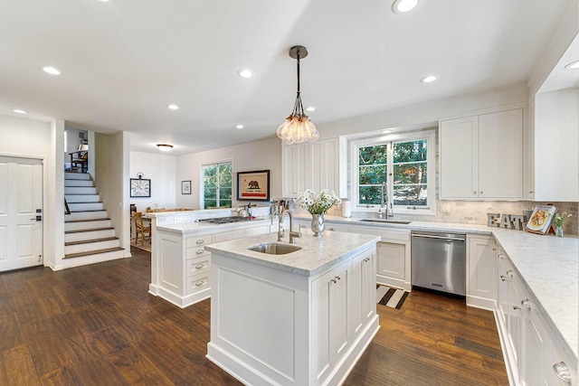 kitchen with a sink, dark wood-type flooring, appliances with stainless steel finishes, and a center island with sink