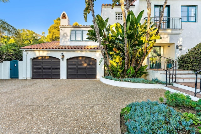 mediterranean / spanish home featuring a balcony, stucco siding, gravel driveway, and a garage