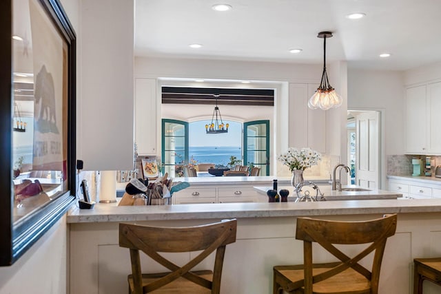 kitchen featuring decorative light fixtures, a breakfast bar area, decorative backsplash, white cabinets, and a sink