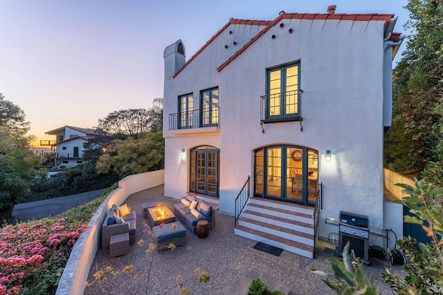 view of front facade with stucco siding, entry steps, french doors, a fire pit, and a balcony