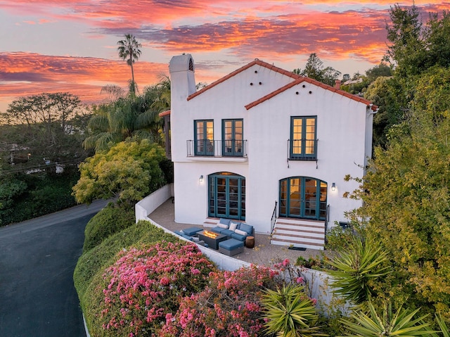 mediterranean / spanish house featuring stucco siding, french doors, a chimney, outdoor lounge area, and a balcony