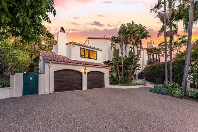 mediterranean / spanish house with stucco siding, driveway, a tile roof, a gate, and a chimney