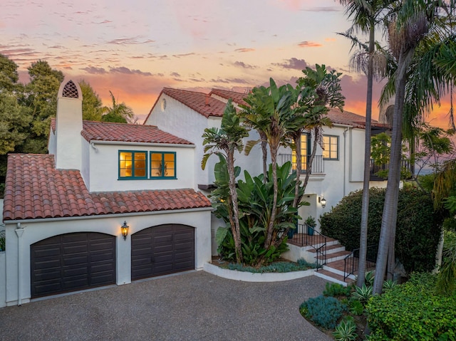 mediterranean / spanish-style house featuring stucco siding, a tiled roof, a chimney, and a garage