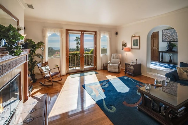 living room with french doors, ornamental molding, a tile fireplace, and light wood-type flooring