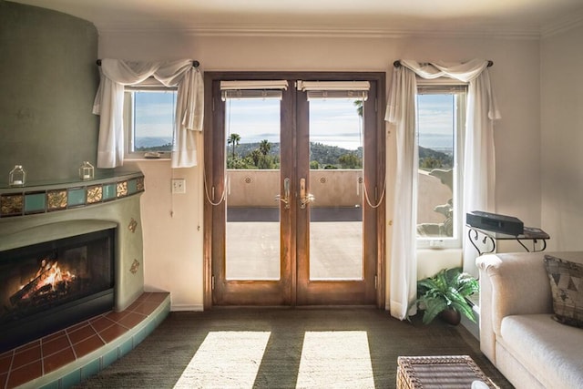 doorway to outside with french doors, crown molding, a tiled fireplace, and dark colored carpet