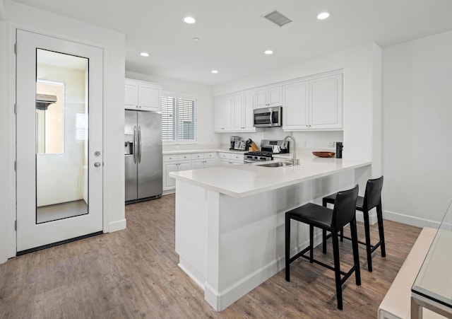 kitchen featuring a kitchen bar, sink, appliances with stainless steel finishes, kitchen peninsula, and white cabinets