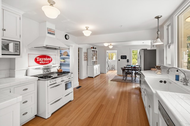 kitchen featuring appliances with stainless steel finishes, tile counters, white cabinets, and island exhaust hood