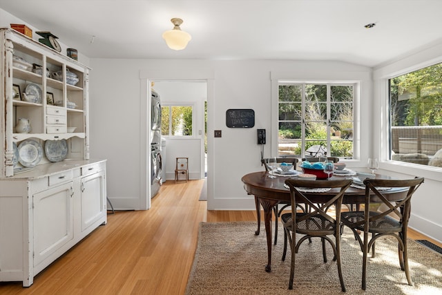 dining area featuring stacked washer and dryer, a wealth of natural light, vaulted ceiling, and light hardwood / wood-style floors