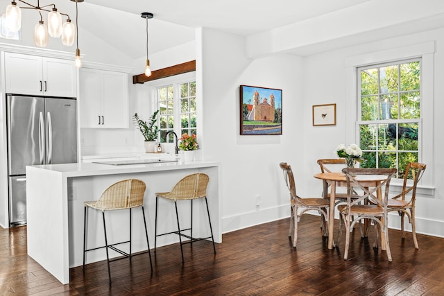 kitchen with kitchen peninsula, vaulted ceiling, stainless steel fridge, hanging light fixtures, and white cabinets