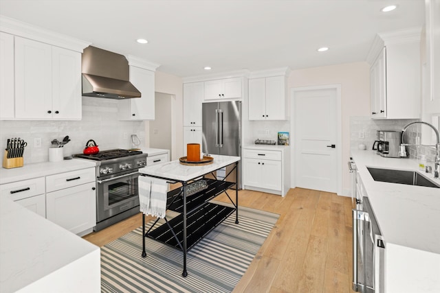 kitchen with sink, white cabinetry, wall chimney range hood, and high quality appliances