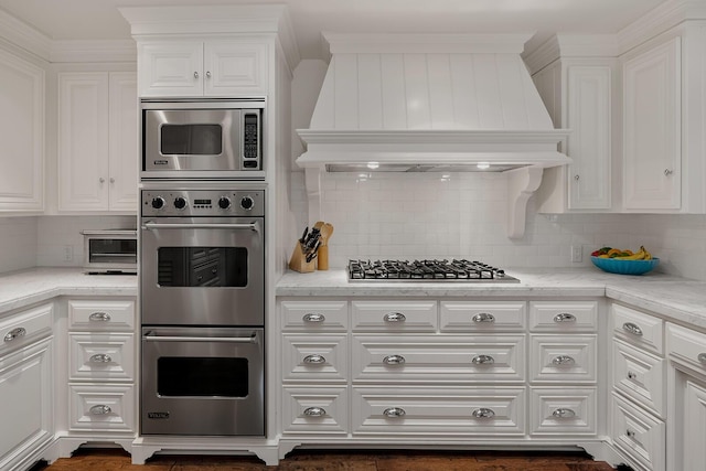 kitchen featuring white cabinets, custom exhaust hood, stainless steel appliances, backsplash, and light stone counters