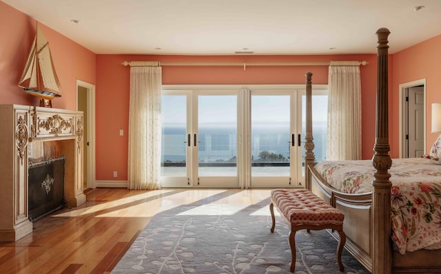 bedroom featuring multiple windows, a water view, light hardwood / wood-style floors, and access to outside