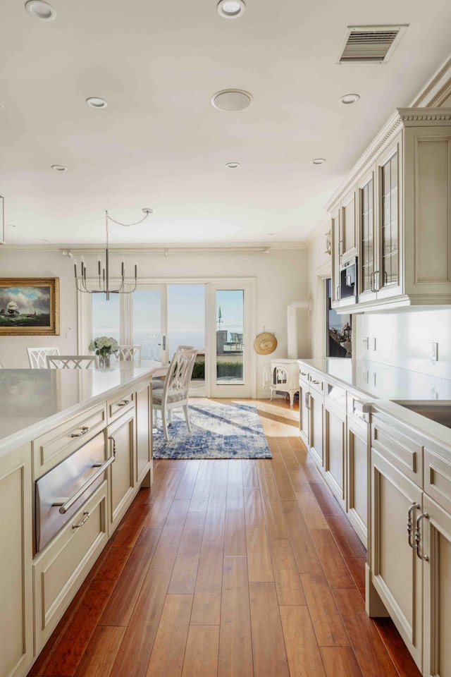 kitchen featuring hardwood / wood-style flooring, pendant lighting, crown molding, and cream cabinetry