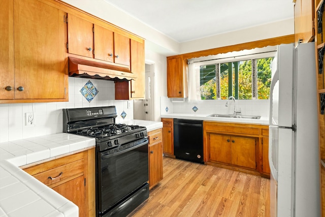 kitchen with sink, backsplash, light hardwood / wood-style floors, black appliances, and tile counters