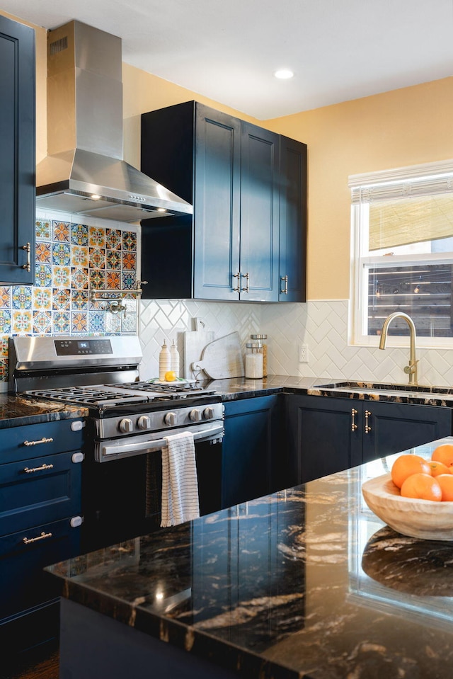 kitchen with sink, blue cabinetry, stainless steel range with gas stovetop, tasteful backsplash, and wall chimney exhaust hood