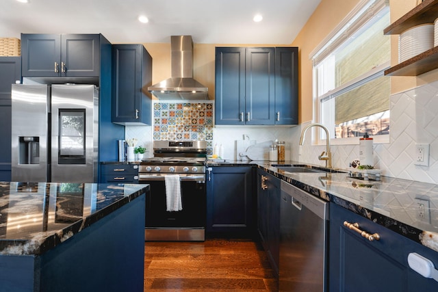 kitchen with appliances with stainless steel finishes, blue cabinets, sink, dark hardwood / wood-style flooring, and wall chimney range hood