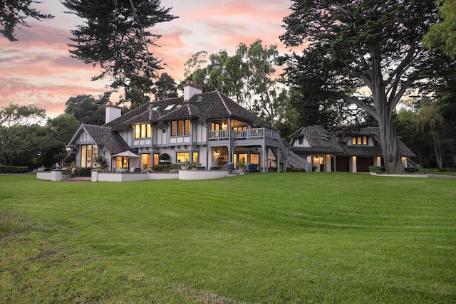 back house at dusk with a patio area and a lawn